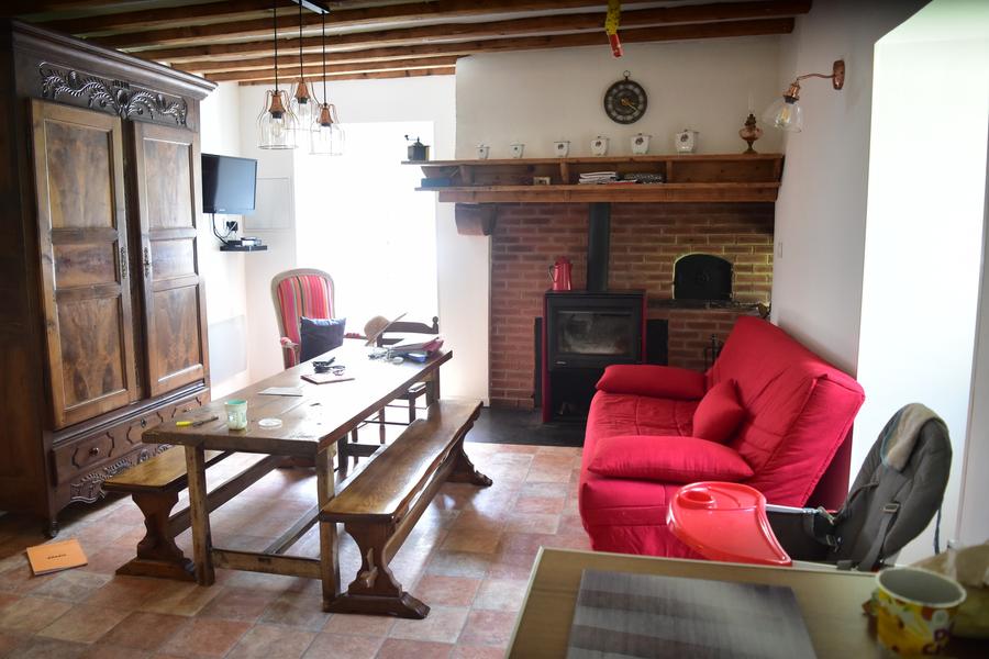 Photo de l'intérieur cozy du gîte : un canapé rouge, une grande table avec des bancs, un poêle.