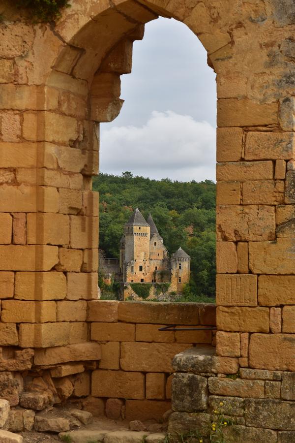 Photo prise depuis la plus haute tour du château de Commarque. On aperçoit un autre château sur une colline au loin, et tout autour un encadrement de fenêtre en pierres, ocres.